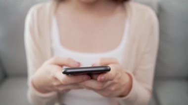 Bir kadın kanepede oturuyor ve cep telefonuna bakıyor. Gülümsüyor ve eğleniyor.