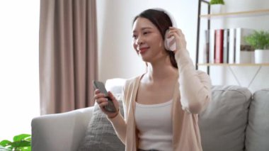 Bir kadın kanepede oturuyor ve müzik dinliyor. Gülümsüyor ve eğleniyor.