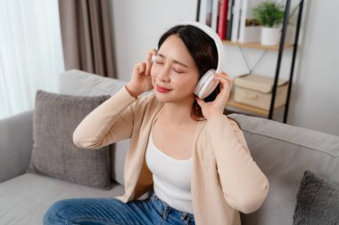 Bir kadın elinde cep telefonuyla kanepede oturuyor. Kulaklık takıyor ve gülümsüyor.