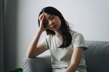 Mutsuz, bunalımlı kadın kanepede oturuyor ve kafasını tutuyor. Üzgün ve yorgun görünüyor..