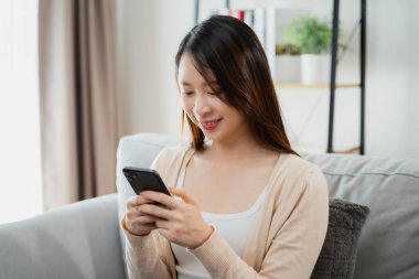 Bir kadın kanepede oturuyor ve cep telefonuna bakıyor. Gülümsüyor ve eğleniyor.