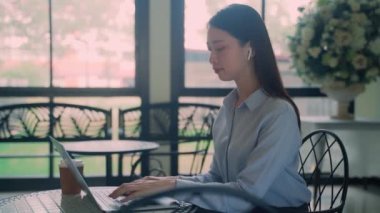 Bir iş kadını bir dizüstü bilgisayar ve bir fincan kahveyle masada oturuyor. İşine odaklanmış ve rahat ve rahat bir ruh hali içinde.