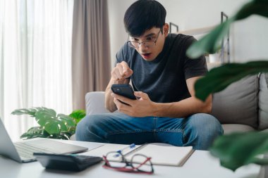 Bir adam elinde cep telefonuyla kanepede oturuyor. O, yüzünde şaşırmış bir ifadeyle telefona bakıyor.