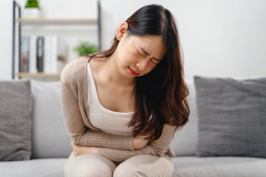 Bir kadın eli karnında bir kanepede oturuyor. Acı çekiyor ve ağlıyor.