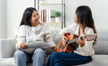 İki kadın bir kanepede oturuyor, biri gitar çalıyor. Gülümsüyorlar ve birbirlerinin arkadaşlığından zevk alıyor gibiler.