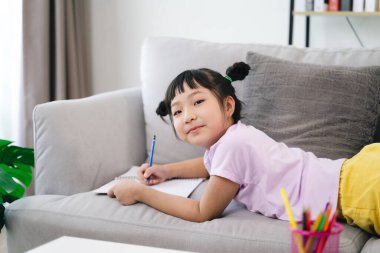 Genç bir kız kanepede oturuyor ve bir deftere yazıyor. Gülümsüyor ve eğleniyor. Sahne bir rahatlama ve rahatlama hissi veriyor.