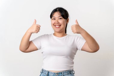 Bir kadın gülümsüyor ve baş parmağını kaldırıyor. Beyaz bir gömlek ve beyaz arka planda izole edilmiş kot pantolon giyiyor..