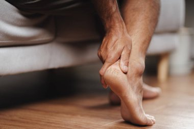 Ayağı desteklenmiş bir adam kanepede oturuyor. Ayakları su topladı ve ovalamaya başladı.