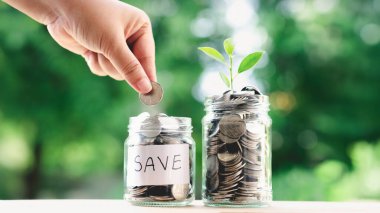 Bir el tasarruf etiketli bir kavanoza bozuk para koyuyor. Para biriktirme kavramı.