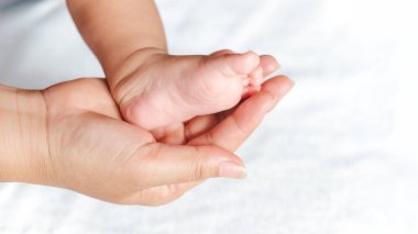 Bir bebeğin ayağı bir annenin elindedir. Bebek küçük ve anne onu nazikçe tutuyor. Anne ve bebek arasındaki sıcaklık ve sevgi kavramı.
