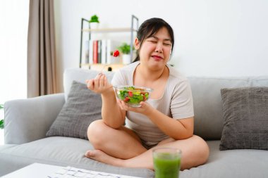 Mutsuz, kilolu bir kadın kasede salata ve bardakta sebze suyu yiyor. Tiksinti ve iğrenme hissi veriyor. Sağlıklı gıda konsepti..
