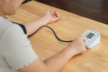 Asyalı bir kadın oturma odasında taşınabilir kan basıncı monitörü kullanıyor. Sağlık farkındalığı kavramı.