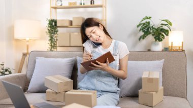 E-ticaret işadamı telefonda sipariş vermeye gelen bir müşteriyle konuşuyor. Kadın teslimat için posta kutusu adresi yazıyor. KOBİ girişimcisi, paketleme kutusu..