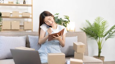 E-ticaret işadamı telefonda sipariş vermeye gelen bir müşteriyle konuşuyor. Kadın teslimat için posta kutusu adresi yazıyor. KOBİ girişimcisi, paketleme kutusu..