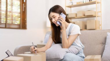 E-ticaret işadamı telefonda sipariş vermeye gelen bir müşteriyle konuşuyor. Kadın teslimat için posta kutusu adresi yazıyor. KOBİ girişimcisi, paketleme kutusu..