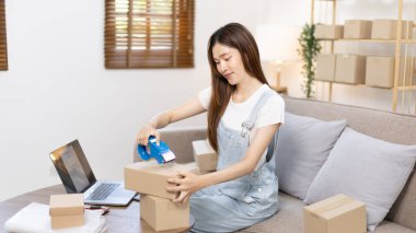 Kadın posta kutusunu paketleyip müşteriye teslim etmeye hazırlanıyor, evde çalışıyor ve işletme sahibi oluyor, çevrimiçi alışveriş yapan KOBİ girişimcisi, paketleme kutusu, çevrimiçi satış, serbest çalışma.