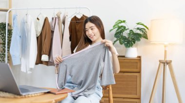 Sosyal medya etkisine sahip güzel bir kadın stüdyosunda ucuz moda kıyafetleri satarak canlı ya da kayıt gösterileri yapıyor, video canlı yayın, Online moda giyim sektörü.