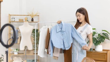 Sosyal medya etkisine sahip güzel bir kadın stüdyosunda ucuz moda kıyafetleri satarak canlı ya da kayıt gösterileri yapıyor, video canlı yayın, Online moda giyim sektörü.