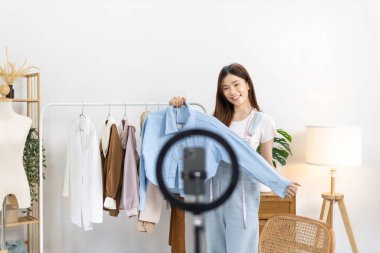 Sosyal medya etkisine sahip güzel bir kadın stüdyosunda ucuz moda kıyafetleri satarak canlı ya da kayıt gösterileri yapıyor, video canlı yayın, Online moda giyim sektörü.