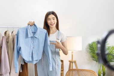Sosyal medya etkisine sahip güzel bir kadın stüdyosunda ucuz moda kıyafetleri satarak canlı ya da kayıt gösterileri yapıyor, video canlı yayın, Online moda giyim sektörü.