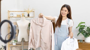 Sosyal medya etkisine sahip güzel bir kadın stüdyosunda ucuz moda kıyafetleri satarak canlı ya da kayıt gösterileri yapıyor, video canlı yayın, Online moda giyim sektörü.