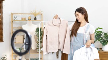 Sosyal medya etkisine sahip güzel bir kadın stüdyosunda ucuz moda kıyafetleri satarak canlı ya da kayıt gösterileri yapıyor, video canlı yayın, Online moda giyim sektörü.