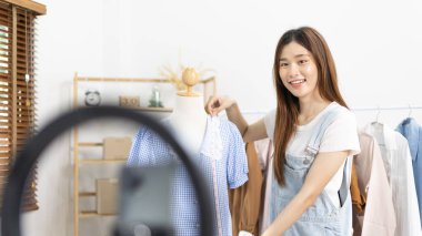 Sosyal medya etkisine sahip güzel bir kadın stüdyosunda ucuz moda kıyafetleri satarak canlı ya da kayıt gösterileri yapıyor, video canlı yayın, Online moda giyim sektörü.