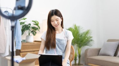 Kadın, internetten ya da uygulamadan sipariş veren müşterilerle sohbet etmek için tablet kullanıyor, evde serbest çalışıyor, kıyafetleri hem perakende hem toptan satıyor, internette satıyor, küçük işletme sahibi, KME girişimcisi.