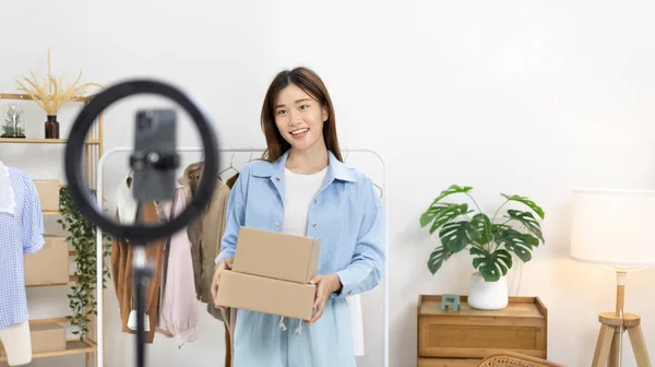 Beautiful woman with a social media influence is greeting the audience for recording vlog video live streaming, Lift the postage box during the live show to confirm the customer\'s order, Online fashion clothing business.