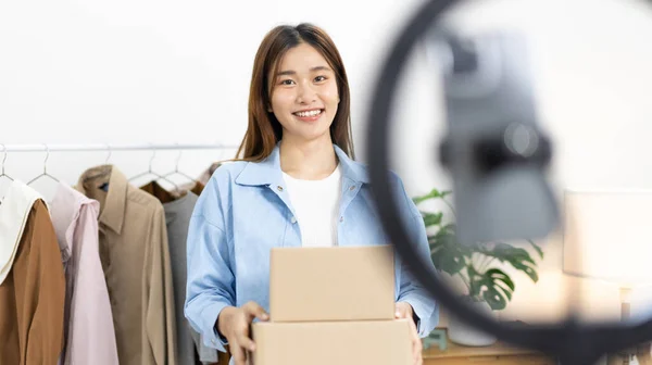 Beautiful woman with a social media influence is greeting the audience for recording vlog video live streaming, Lift the postage box during the live show to confirm the customer\'s order, Online fashion clothing business.