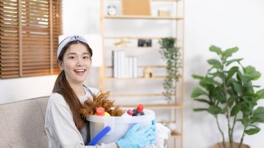 Önlük ve temizlik eldivenleri giyen güzel Asyalı ev hanımı evini, ev işlerini, günlük rutinini, büyük temizliği, evdeki mikropları temizleyip temizlemeye hafta sonları temizlik yapmaya hazırlanıyor..