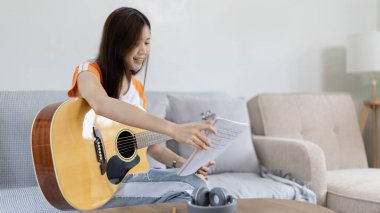 Gitar çalmayı öğrenen ya da pratik yapan bir kadın, parmaklarını gitar akorlarını tutmak için kullanıyor, notalara bilerek bakıyor, boş zamanlarından faydalanıyor, boş zamanlarında rahatlıyor..