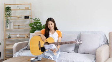 Gitar çalmayı öğrenen ya da pratik yapan bir kadın, parmaklarını gitar akorlarını tutmak için kullanıyor, notalara bilerek bakıyor, boş zamanlarından faydalanıyor, boş zamanlarında rahatlıyor..