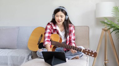 Gitar çalmayı öğrenen ya da pratik yapan bir kadın, parmaklarını gitar akorlarını tutmak için kullanıyor, notalara bilerek bakıyor, boş zamanlarından faydalanıyor, boş zamanlarında rahatlıyor..