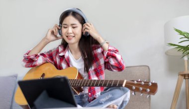 Gitar çalmayı öğrenen ya da pratik yapan bir kadın, parmaklarını gitar akorlarını tutmak için kullanıyor, notalara bilerek bakıyor, boş zamanlarından faydalanıyor, boş zamanlarında rahatlıyor..