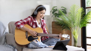 Gitar çalmayı öğrenen ya da pratik yapan bir kadın, parmaklarını gitar akorlarını tutmak için kullanıyor, notalara bilerek bakıyor, boş zamanlarından faydalanıyor, boş zamanlarında rahatlıyor..