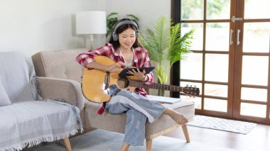 Gitar çalmayı öğrenen ya da pratik yapan bir kadın, parmaklarını gitar akorlarını tutmak için kullanıyor, notalara bilerek bakıyor, boş zamanlarından faydalanıyor, boş zamanlarında rahatlıyor..
