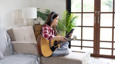 Gitar çalmayı öğrenen ya da pratik yapan bir kadın, parmaklarını gitar akorlarını tutmak için kullanıyor, notalara bilerek bakıyor, boş zamanlarından faydalanıyor, boş zamanlarında rahatlıyor..