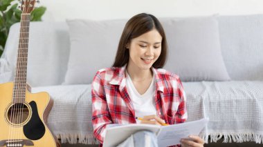 Asyalı kadın, müzik konusunda uzmanlaşmış, yeni bir single 'ın açılışı için şarkı sözlerini ve melodileri bestelemekte, müzik, akustik gitar, müzik notaları oluşturmada hayal gücünü ve konsantrasyonu kullanmaktadır..