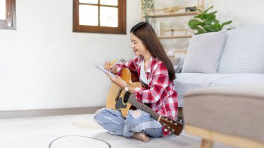 Asyalı kadın, müzik konusunda uzmanlaşmış, yeni bir single 'ın açılışı için şarkı sözlerini ve melodileri bestelemekte, müzik, akustik gitar, müzik notaları oluşturmada hayal gücünü ve konsantrasyonu kullanmaktadır..