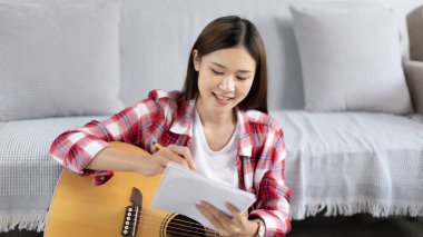 Asyalı kadın, müzik konusunda uzmanlaşmış, yeni bir single 'ın açılışı için şarkı sözlerini ve melodileri bestelemekte, müzik, akustik gitar, müzik notaları oluşturmada hayal gücünü ve konsantrasyonu kullanmaktadır..