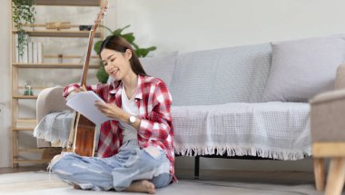 Asyalı kadın, müzik konusunda uzmanlaşmış, yeni bir single 'ın açılışı için şarkı sözlerini ve melodileri bestelemekte, müzik, akustik gitar, müzik notaları oluşturmada hayal gücünü ve konsantrasyonu kullanmaktadır..