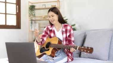 Oturma odasındaki dizüstü bilgisayarda gitar çalan ve canlı ya da canlı yayın yapan kadın sanatçı, müzik terapisiyle rahatlama, izleyicilere ya da fan kulüplerine keyif ve eğlence sunma, müzik, akustik gitar.