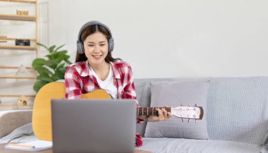 Oturma odasındaki dizüstü bilgisayarda gitar çalan ve canlı ya da canlı yayın yapan kadın sanatçı, müzik terapisiyle rahatlama, izleyicilere ya da fan kulüplerine keyif ve eğlence sunma, müzik, akustik gitar.