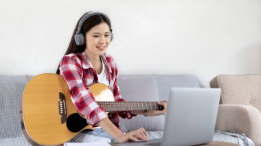 Oturma odasındaki dizüstü bilgisayarda gitar çalan ve canlı ya da canlı yayın yapan kadın sanatçı, müzik terapisiyle rahatlama, izleyicilere ya da fan kulüplerine keyif ve eğlence sunma, müzik, akustik gitar.