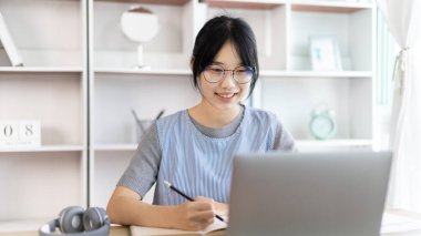 Not defterine not alan Asyalı kadın evde dizüstü bilgisayarda çalışırken, görüntülü sohbet, online iletişim, Evde kal, Yeni Normal, Mesafeli Öğrenme