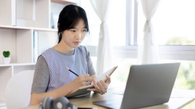 Not defterine not alan Asyalı kadın evde dizüstü bilgisayarda çalışırken, görüntülü sohbet, online iletişim, Evde kal, Yeni Normal, Mesafeli Öğrenme