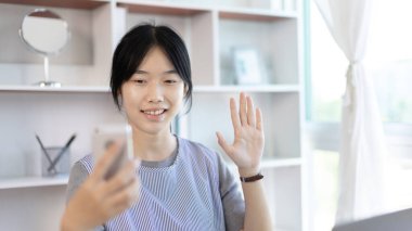 Genç Asyalı kadınlar video sohbetleri yoluyla arkadaşlarını ve öğretmenlerini selamlıyor ve onları neşeli ifadelerle karşılıyor, İnternet iletişimi, Evde kal, Yeni Normal, VDO Çağrısı, Sosyal Mesafe, İnternet öğrenimi.