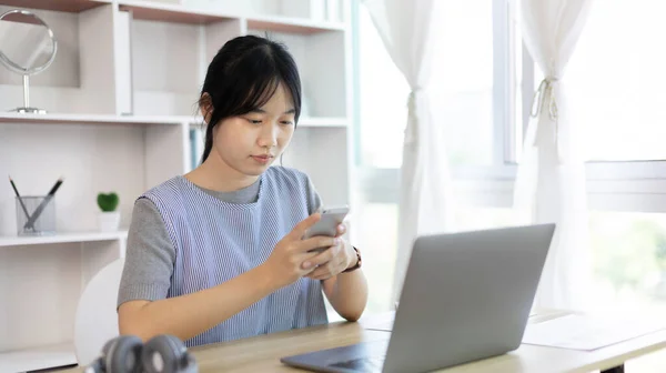 Asian woman having fun playing games on mobile phone, Play games on the sofa in the living room on weekends, Resting at home, Comfort zone, Touch screen mobile phone.