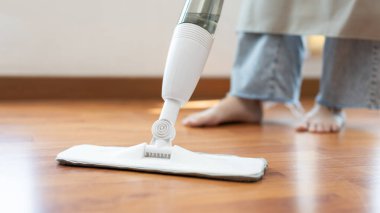 Genç ev hanımı ahşap zemini paspaslıyor ve temizliyor oturma odasını temizlemek için antiseptik paspas kullanıyor ev ödevlerini yapıyor ev kadınlarının görevlerini yapıyor profesyonel sağlık hizmetleri kavramını kullanıyor..